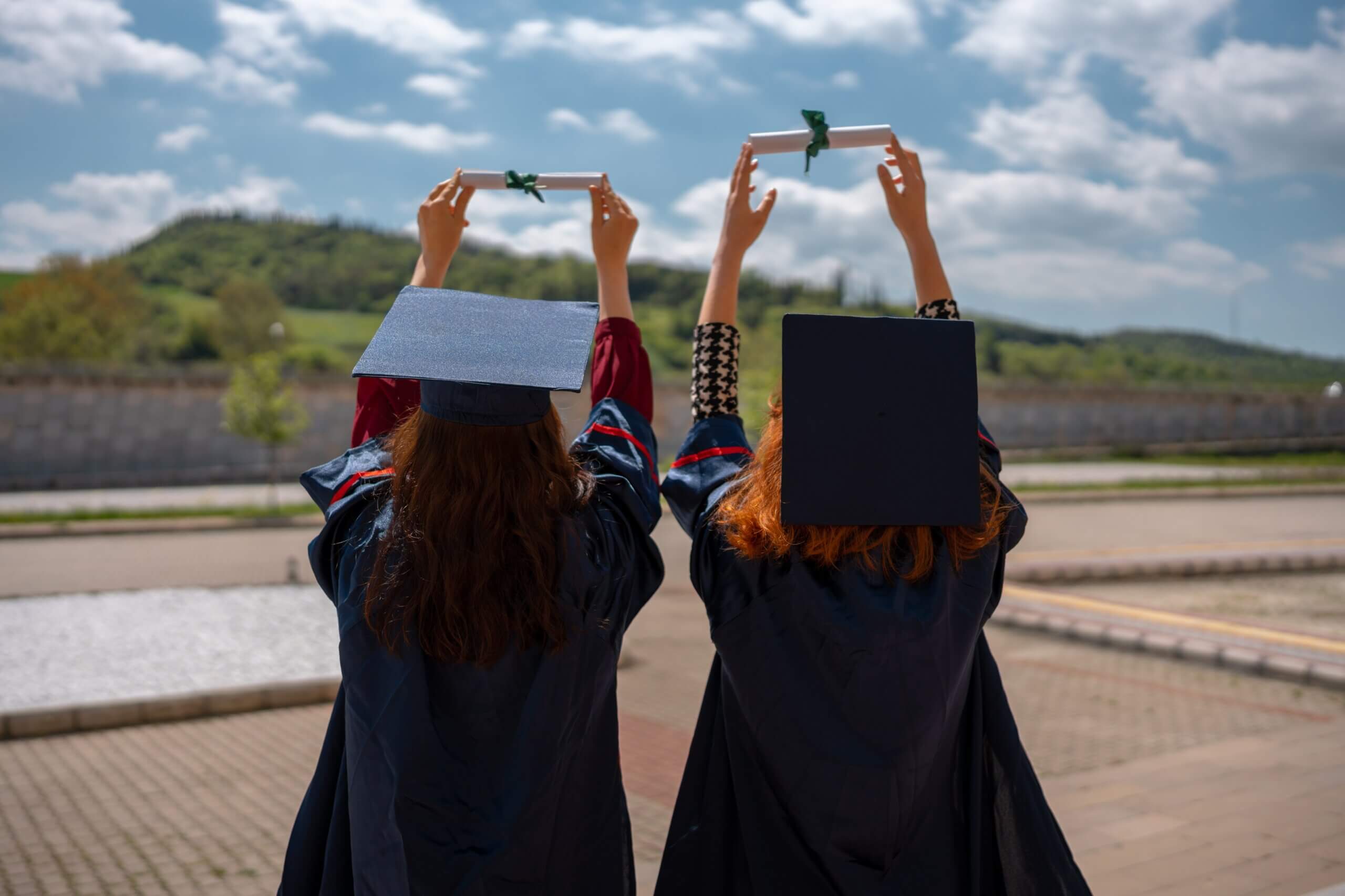 Two students holding up diplomas in graduation gowns