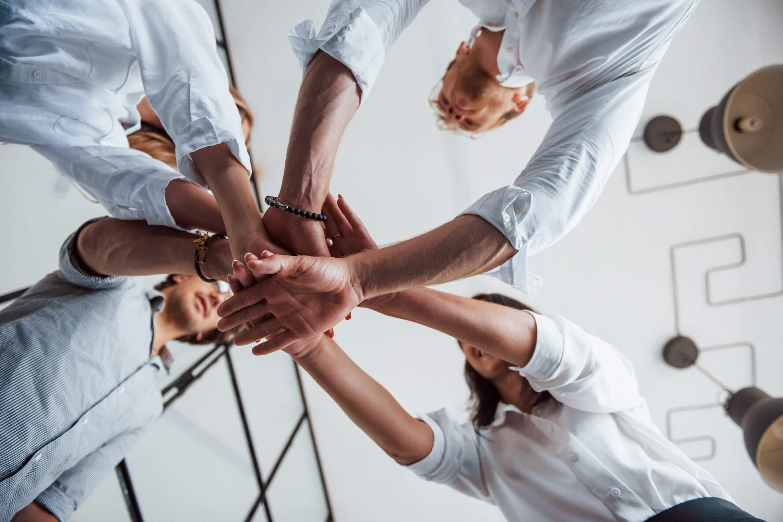 People dressed in white in a circle placing hands together in a huddle