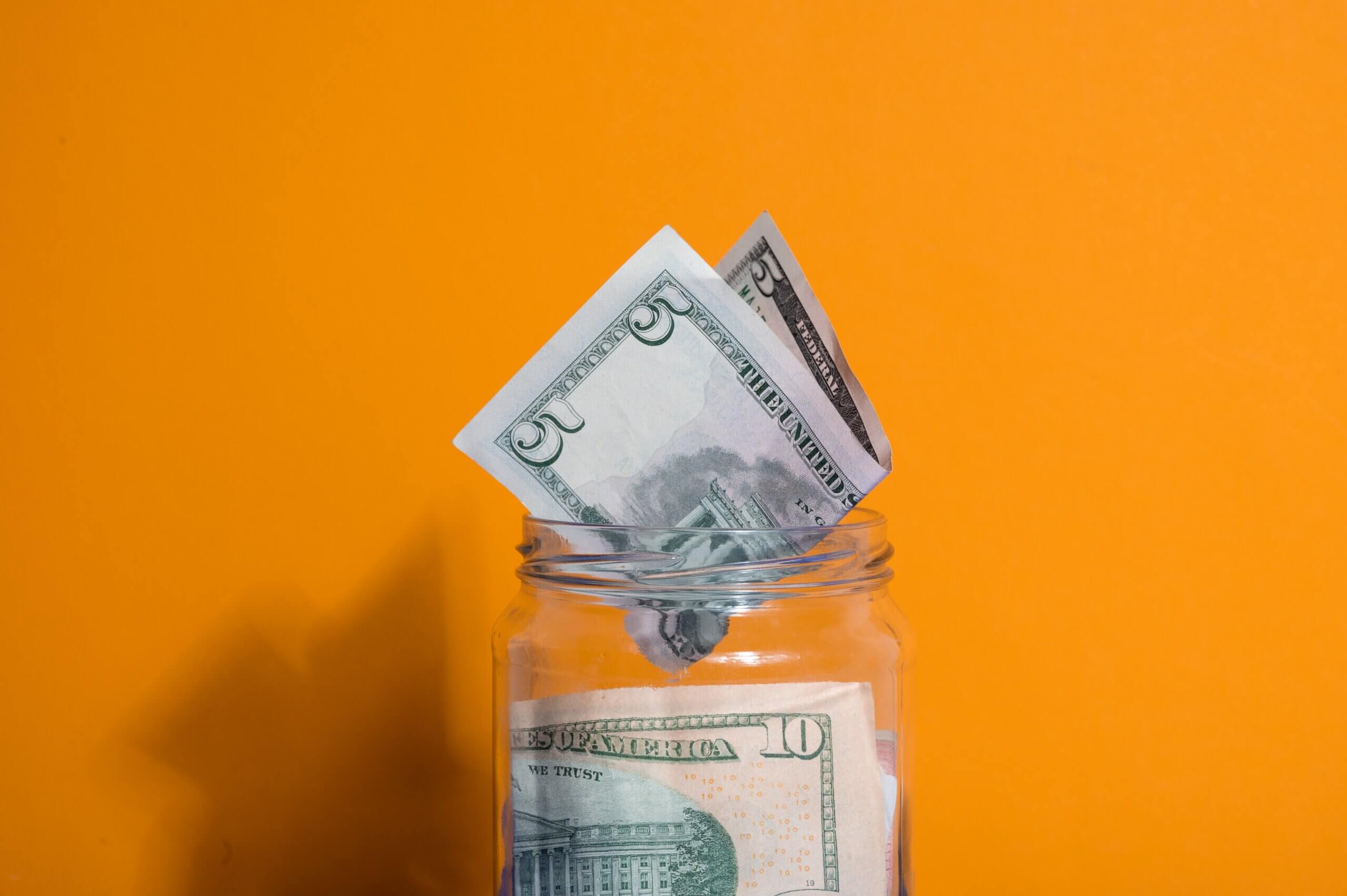 A $5 dollar bill going into a jar of money