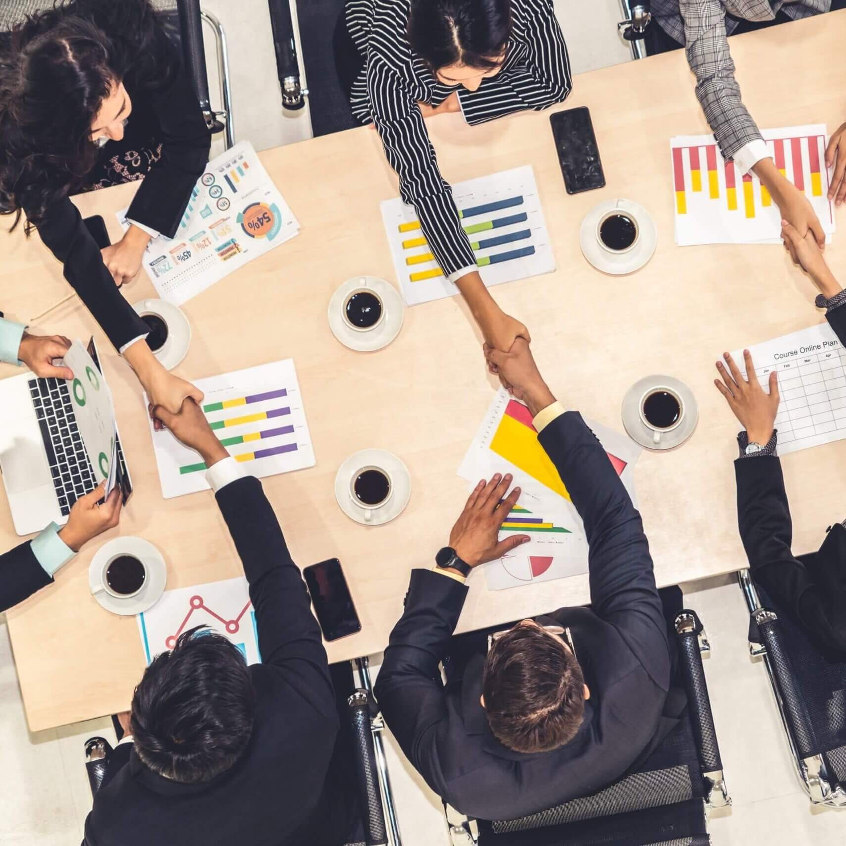 People in suits shaking hands while sitting at a table.